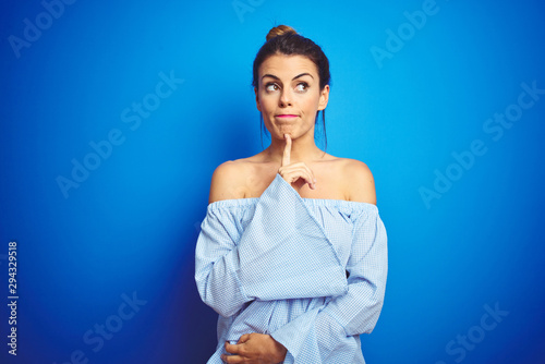 Young beautiful woman wearing bun hairstyle over blue isolated background Thinking concentrated about doubt with finger on chin and looking up wondering