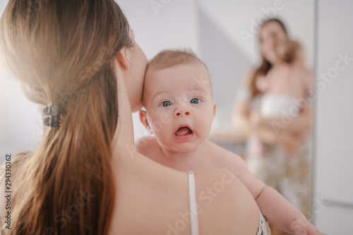 Close up of Caucasian mother holding her loving six months old son. Baby looking at camera with confused facial expression.