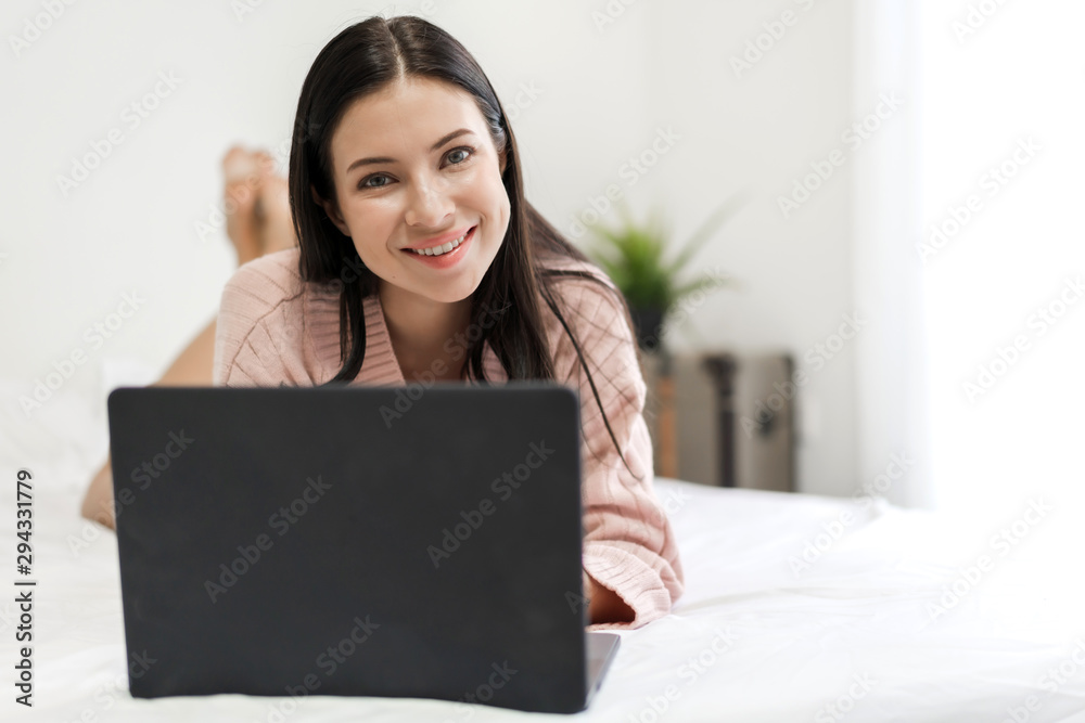 Young woman relaxing using laptop computer on a cold winter day in the bedroom.woman checking social apps and working.Communication and technology concept Young woman relaxing using laptop computer on a cold winter day in the bedroom.woman checking social apps and working.Communication and technology concept