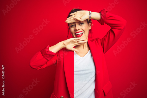 Fényképezés Young beautiful business woman standing over red isolated background Smiling cheerful playing peek a boo with hands showing face