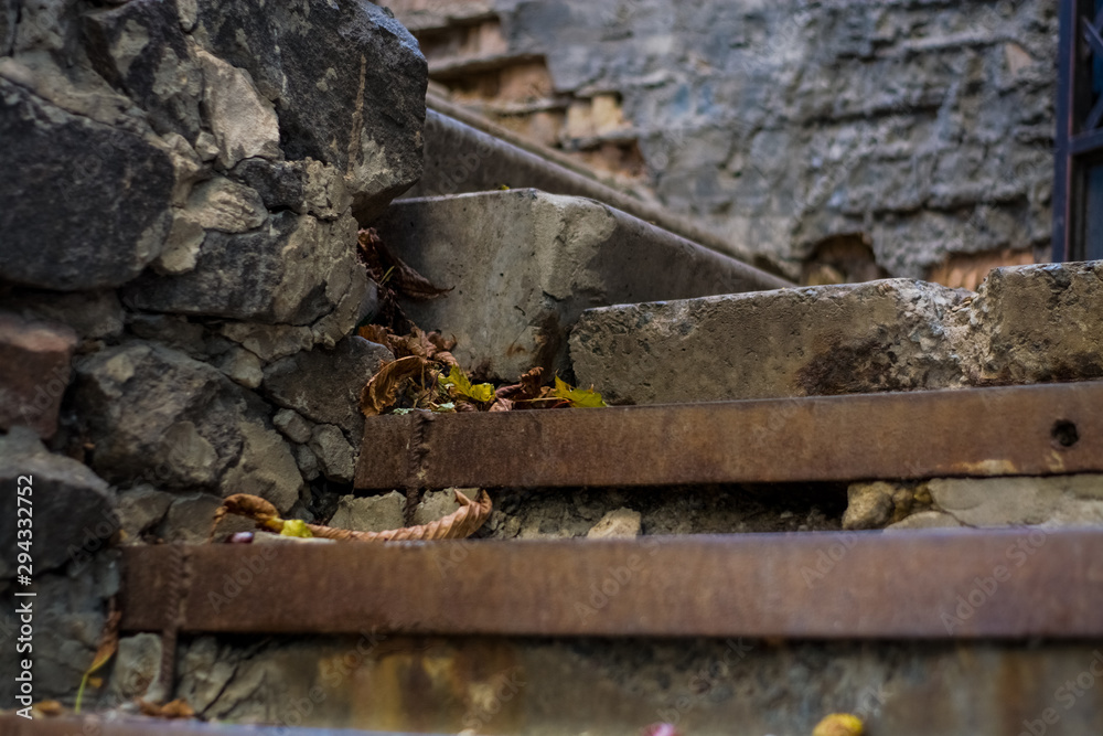 Background or texture of broken old, concrete steps on street with metal crossbars and fallen autumn, yellow leaves. Stone wall. Background or texture of broken old, concrete steps on street with metal crossbars and fallen autumn, yellow leaves. Stone wall.