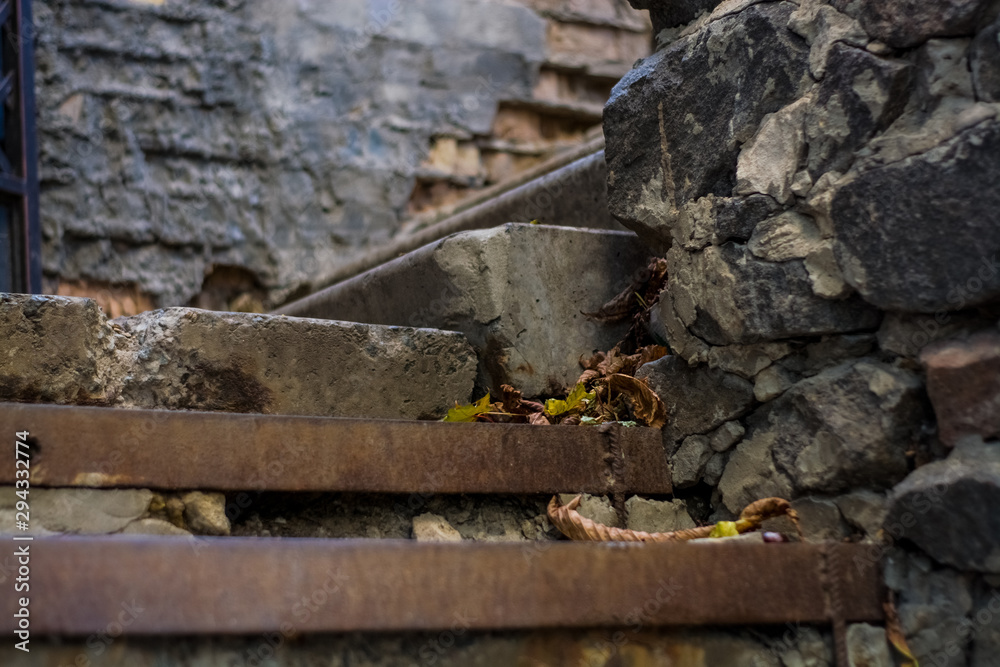 Background or texture of broken old, concrete steps on street with metal crossbars and fallen autumn, yellow leaves. Stone wall. Background or texture of broken old, concrete steps on street with metal crossbars and fallen autumn, yellow leaves. Stone wall.
