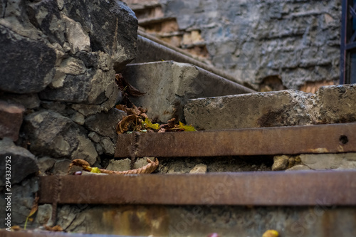 Background or texture of broken old, concrete steps on street with metal crossbars and fallen autumn, yellow leaves. Stone wall. © Vlada
