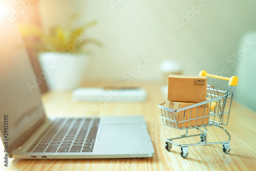 Fototapeta Brown paper boxs in a shopping cart with laptop keyboard on wood table in office background