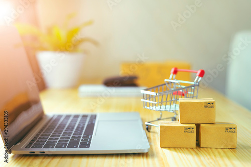 Brown paper boxs and a shopping cart with laptop keyboard on wood table in office background.Easy shopping with finger tips for consumers.Online shopping and delivery service concept.