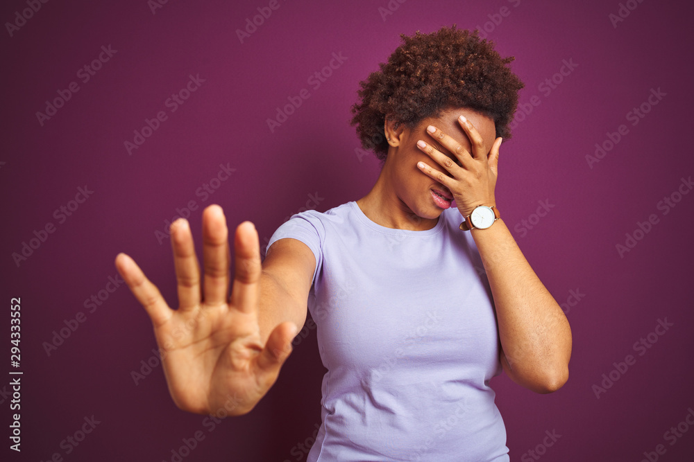 Young beautiful african american woman with afro hair over isolated purple background covering eyes with hands and doing stop gesture with sad and fear expression. Embarrassed and negative concept. Young beautiful african american woman with afro hair over isolated purple background covering eyes with hands and doing stop gesture with sad and fear expression. Embarrassed and negative concept.