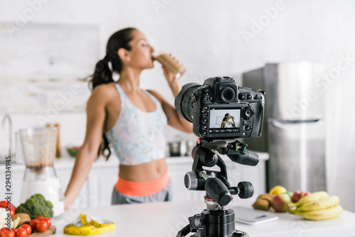 selective focus of digital camera with girl drinking smoothie near fruits and vegetables on screen