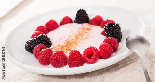 raspberries and blackberries laid out on a white plate in circle with yogurt and cinnamon