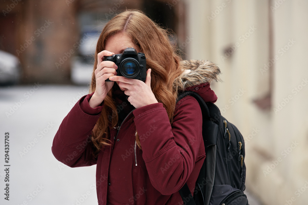 Young attractive woman photographer taking photos in winter city