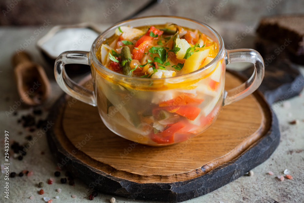 Appetizing soup with vegetables and meat in a transparent plate on a gray background