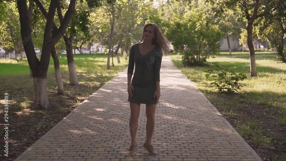 Cute young girl in the park among the trees. A happy girl in a gray dress is dancing, jumping, having fun and fooling around. Cute young girl in the park among the trees. A happy girl in a gray dress is dancing, jumping, having fun and fooling around.