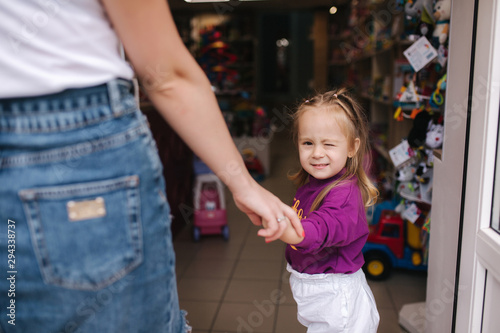 Cute little girl with her mom go into toy store. Happy kid choosing toys with mother. Mom and daughter buying toys in kids store