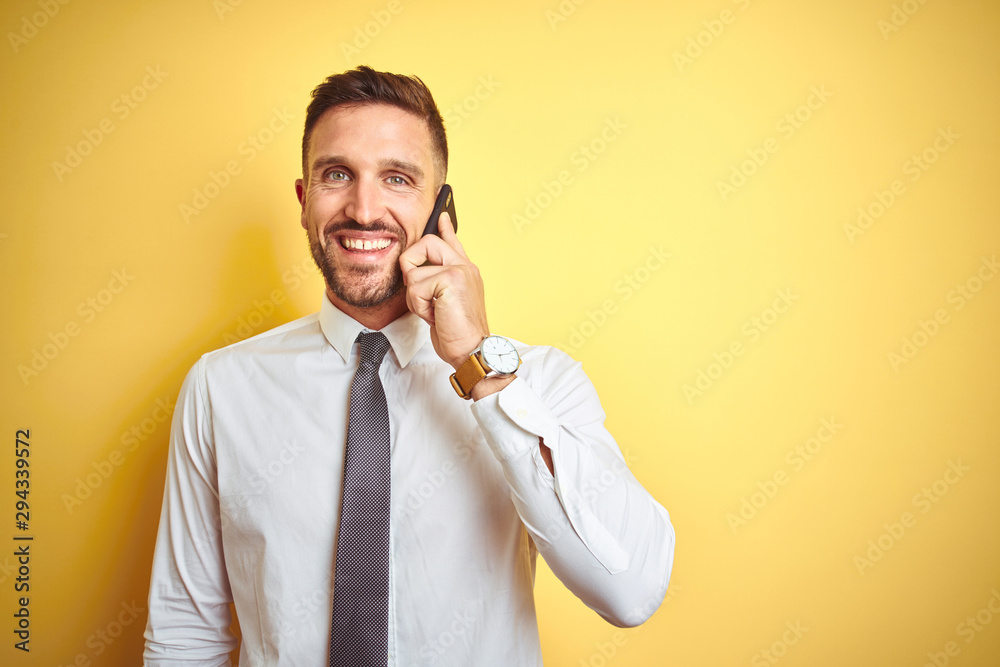 Young handsome business man talking on the phone over yellow isolated background with a happy face standing and smiling with a confident smile showing teeth Young handsome business man talking on the phone over yellow isolated background with a happy face standing and smiling with a confident smile showing teeth