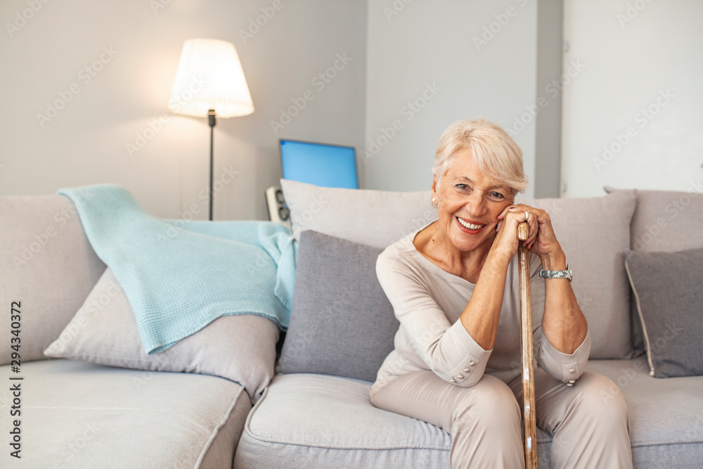 Elderly woman with walking stick at home. Caucasian female looking at camera and smiling. Happy senior woman with walking stick seating at home. It's a long road to recovery Elderly woman with walking stick at home. Caucasian female looking at camera and smiling. Happy senior woman with walking stick seating at home. It's a long road to recovery