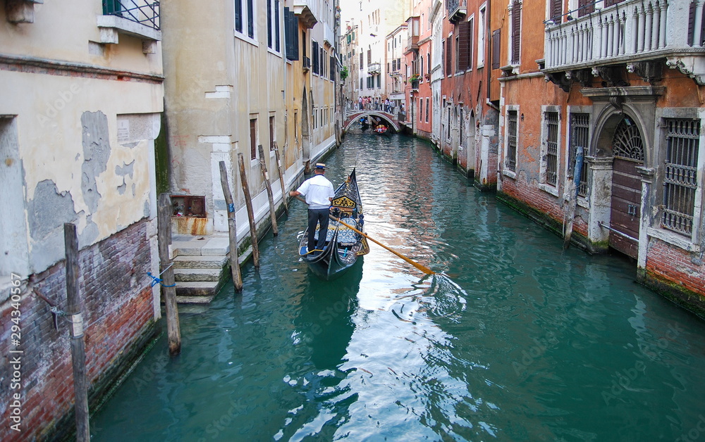 Undefined gondolier operate gondola through the narrow canal of Venice. Italy