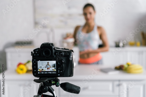 selective focus of digital camera with happy woman gesturing near blender on screen