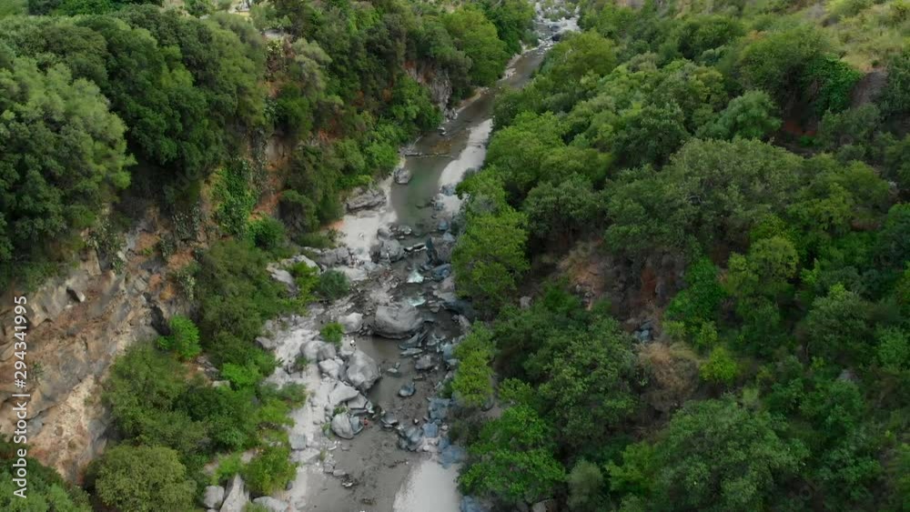 4K AERIAL DOLLY IN: Drone flying above Alcantara Gorges, an impressive channel of lava columns eroded naturally into ravines, canyons and caves. A view over the river and its crystal water and trees