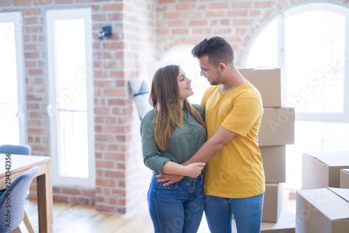 Young beautiful couple in love around cardboard boxes moving to new home, smiling very happy and cheerful for new apartment