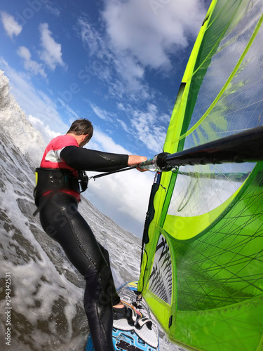Windsurfing in the wave of the North Sea. Man with windsurfer and wetsuit in sunny weather in front of a wave in the North Sea.