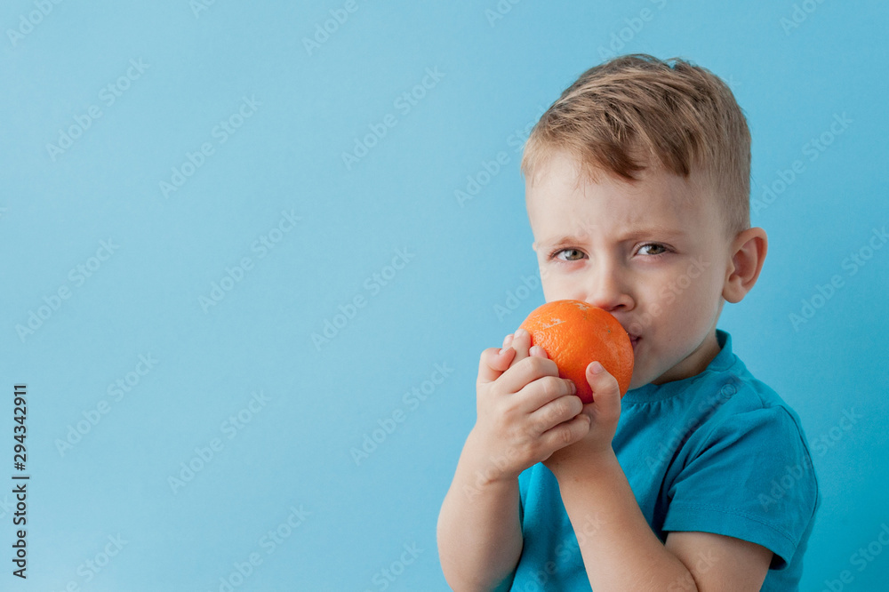 Little Boy Holding an Orange in his hands on blue background, diet and exercise for good health concept Little Boy Holding an Orange in his hands on blue background, diet and exercise for good health concept