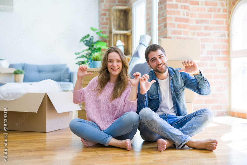 Young beautiful couple moving to a new house sitting on the floor looking confident with smile on face, pointing oneself with fingers proud and happy.