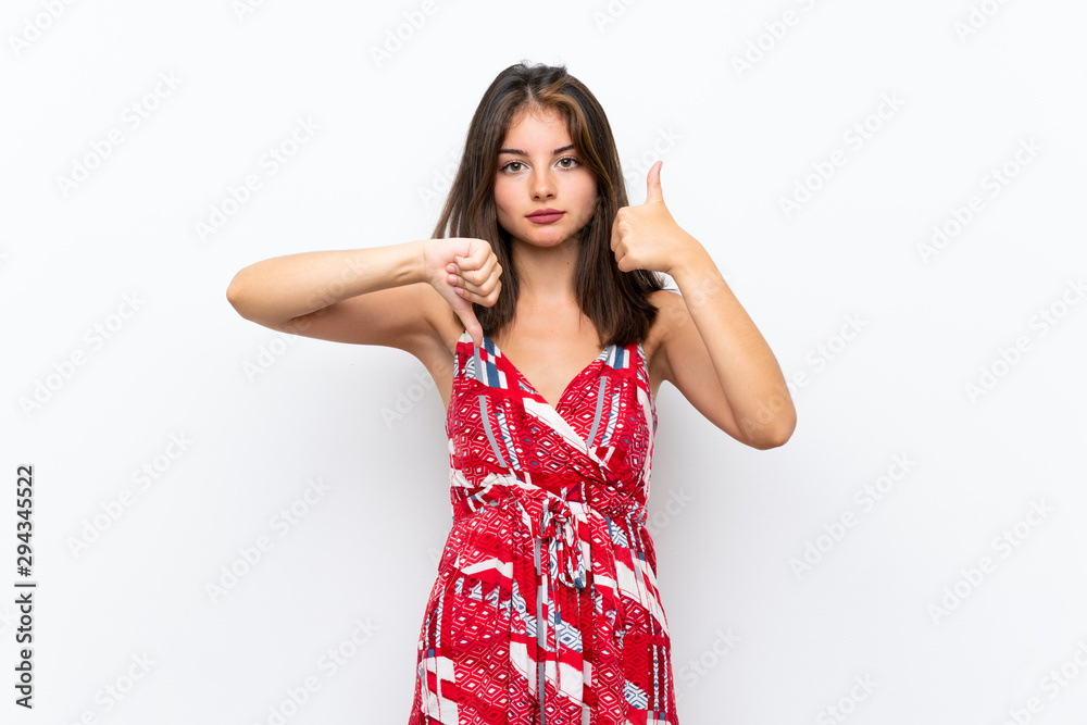 Caucasian girl in red dress over isolated white wall making good-bad sign. Undecided between yes or not Caucasian girl in red dress over isolated white wall making good-bad sign. Undecided between yes or not