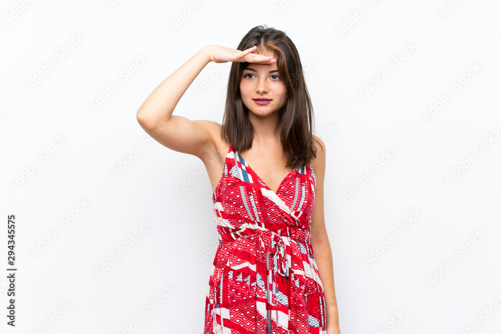 Caucasian girl in red dress over isolated white wall looking far away with hand to look something Caucasian girl in red dress over isolated white wall looking far away with hand to look something