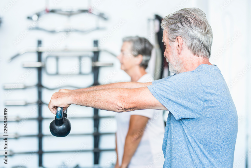 two seniors working her body to be healthy together at the gym holding a weight - couple of mature people training