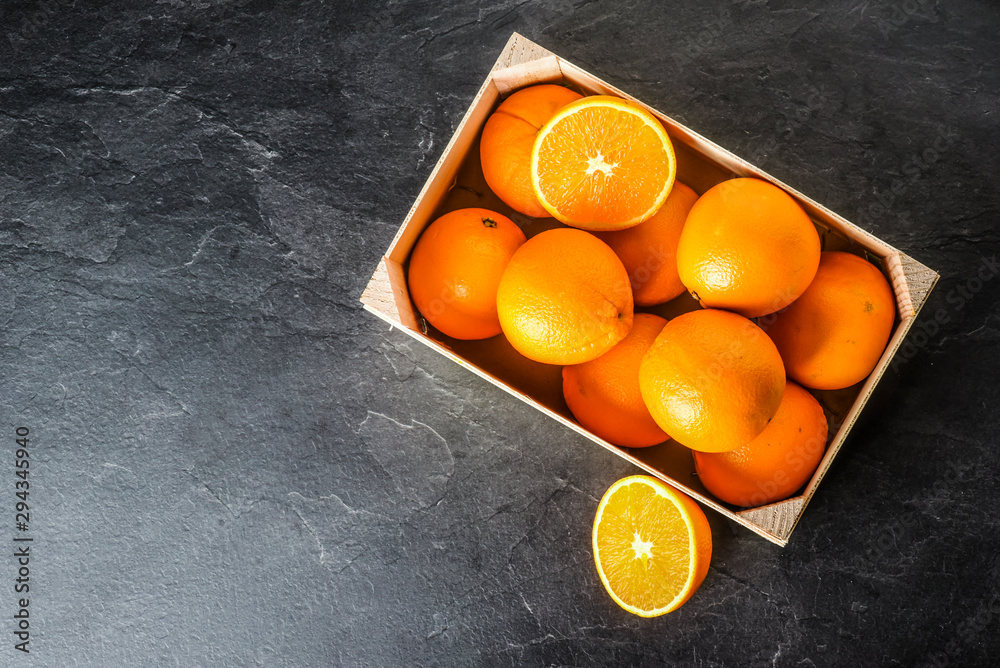 Orange fruits in wooden box on dark stone table. Heap of oranges in box.  Fresh juicy orange from top view.
