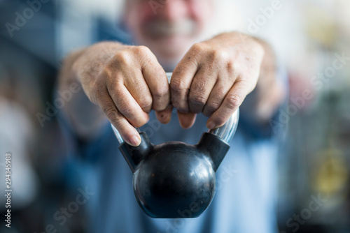 close up of senior holding a weight with his hands in front of the camera at the gym - adult man working his body to be healthy photo