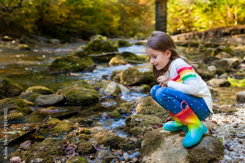 Outdoor recreation and awesome adventures with kids. A little child girl is walking along a green river in the forest in rubber boots on a warm autumn day.  exploring nature, travel, family vacation.