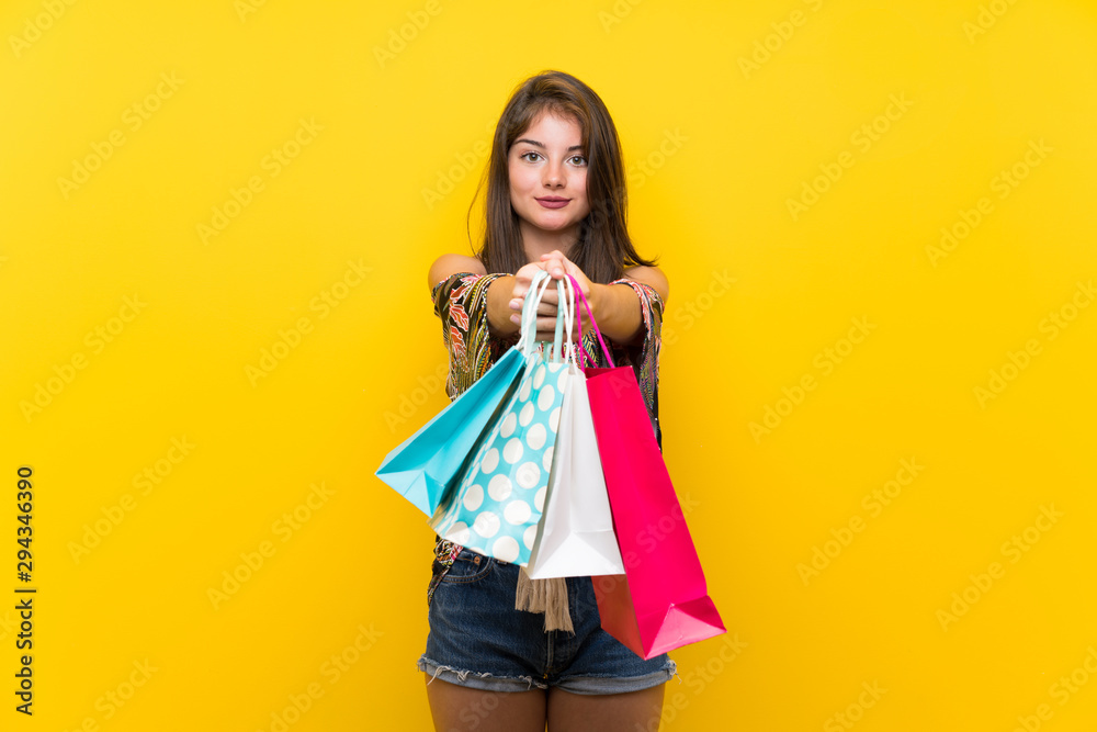 Caucasian girl in colorful dress over isolated yellow background holding a lot of shopping bags