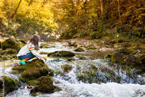 Outdoor recreation and awesome adventures with kids. A little child girl is walking along a green river in the forest in rubber boots on a warm autumn day. exploring nature, travel, family vacation.