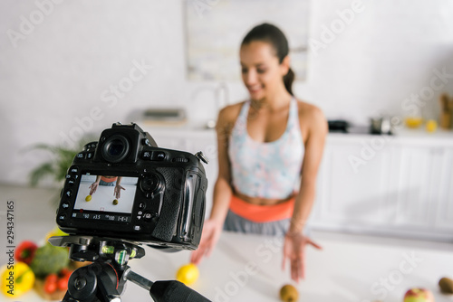 selective focus of digital camera with lemon and kiwi near woman on screen