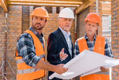 constructors holding blueprint near mature businessman in suit