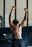 Happy fit man with defined abdominal muscules laughing and rising arms up in the air after finishing working out in gym