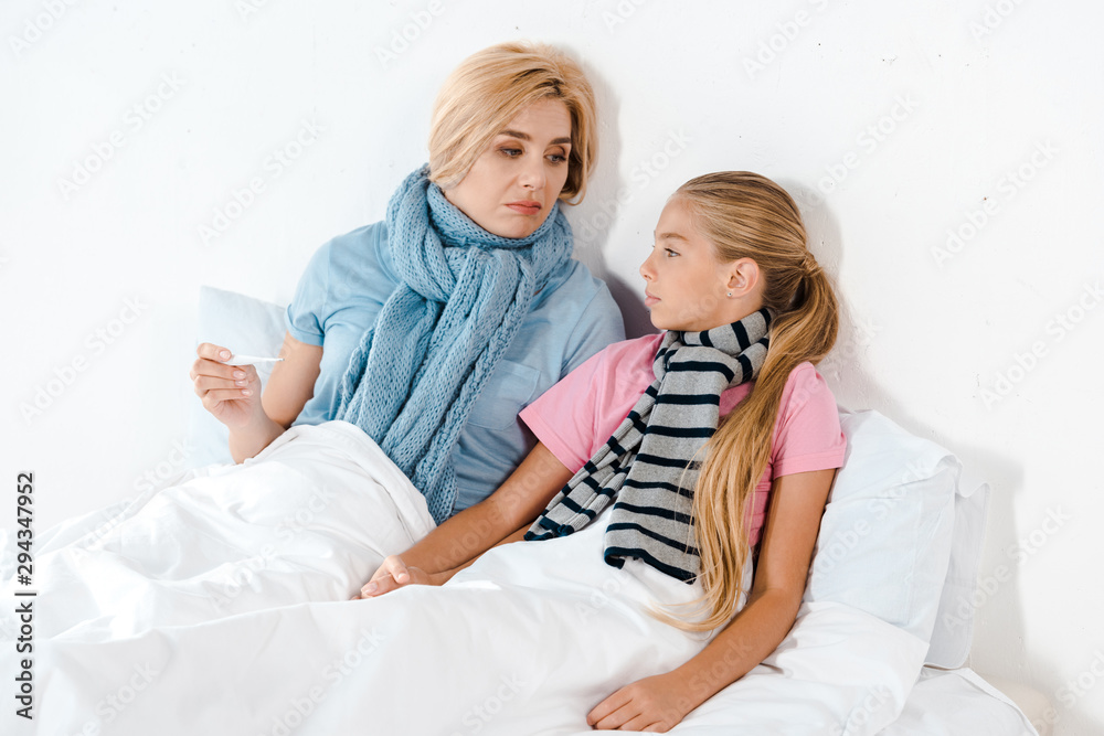 ill mother holding digital thermometer and looking at daughter ill mother holding digital thermometer and looking at daughter
