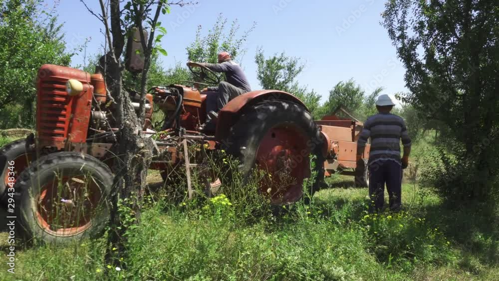 Two farmers work in small field baling hay with ancient tractor and baler. Two farmers work in small field baling hay with ancient tractor and baler.