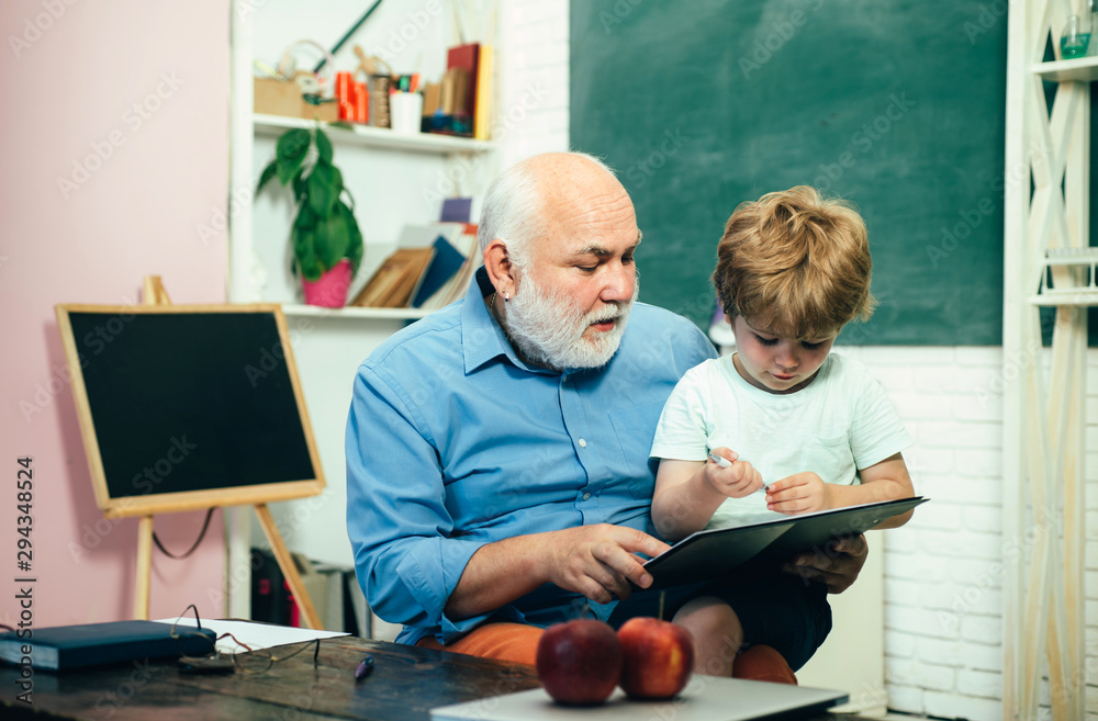 Teacher and pupil learning together in school. Educational process. Grandfather with grandson learning together. - obrazy, fototapety, plakaty 