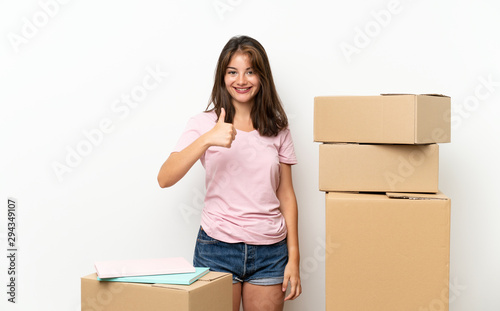 Young girl moving in new home among boxes giving a thumbs up gesture © luismolinero