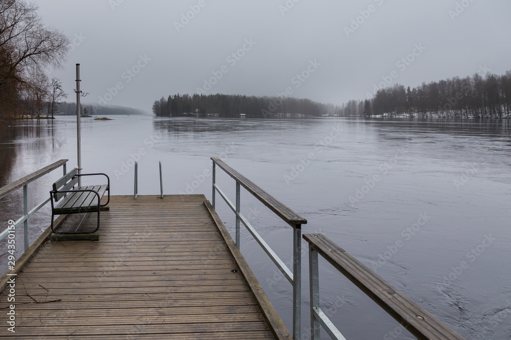 Small pier at beach on Lake Ruotsalainen at cloudy, winter day, Finland.