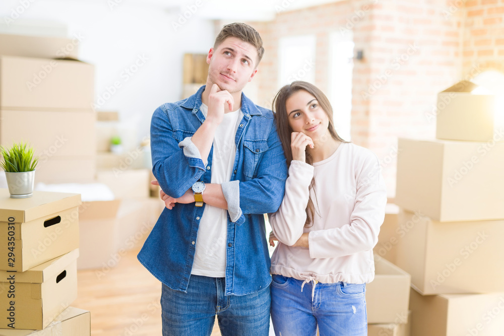 Beautiful young couple moving to a new house with hand on chin thinking about question, pensive expression. Smiling with thoughtful face. Doubt concept. Beautiful young couple moving to a new house with hand on chin thinking about question, pensive expression. Smiling with thoughtful face. Doubt concept.