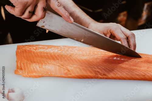 Professional chef preparing a fresh salmon on a cutting board.