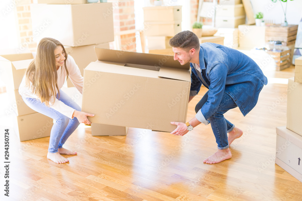Beautiful young couple smiling in love holding a big cardboard box, happy for moving to a new home Beautiful young couple smiling in love holding a big cardboard box, happy for moving to a new home
