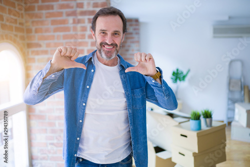 Middle age senior man moving to a new house packing cardboard boxes looking confident with smile on face, pointing oneself with fingers proud and happy.