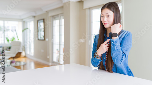 Young beautiful asian woman with long hair wearing denim jacket In hurry pointing to watch time, impatience, looking at the camera with relaxed expression