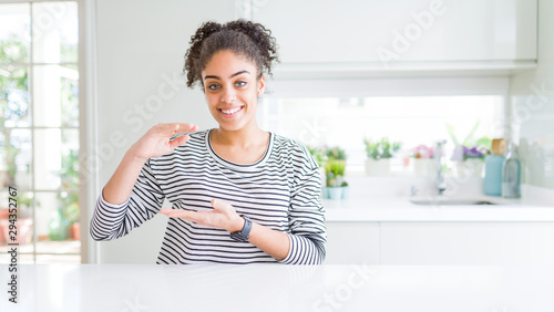 Beautiful african american woman with afro hair wearing casual striped sweater gesturing with hands showing big and large size sign  measure symbol. Smiling looking at the camera. Measuring concept.