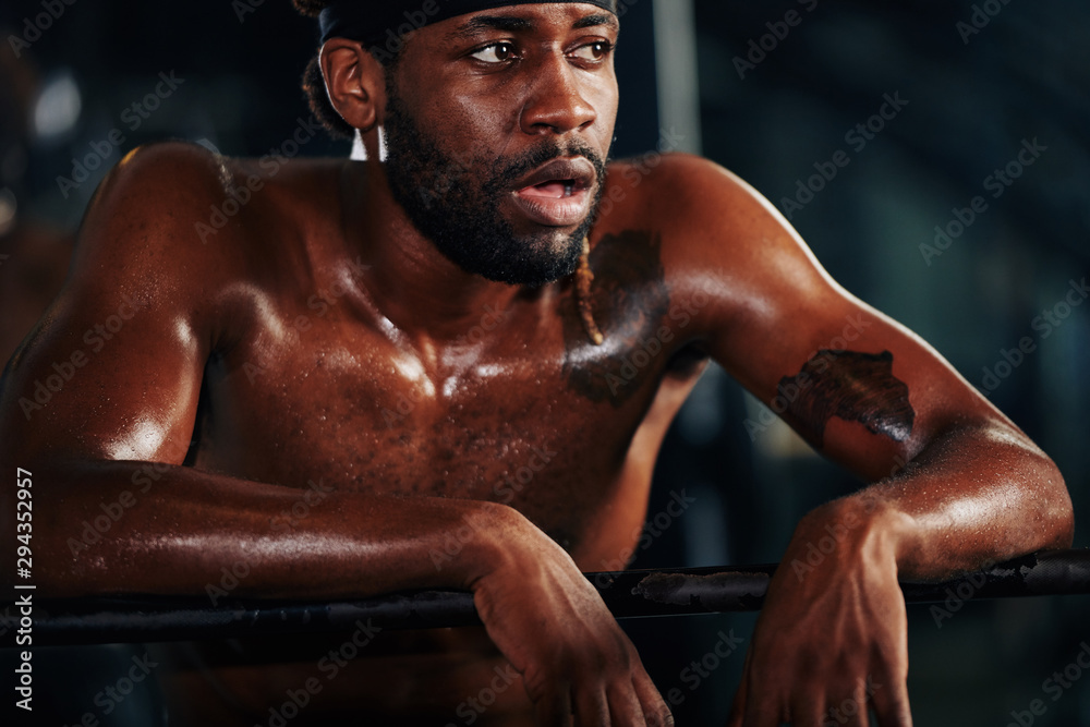 Tired heavy breathing sportsman leaning on gym facility to get some rest between sets of exercise