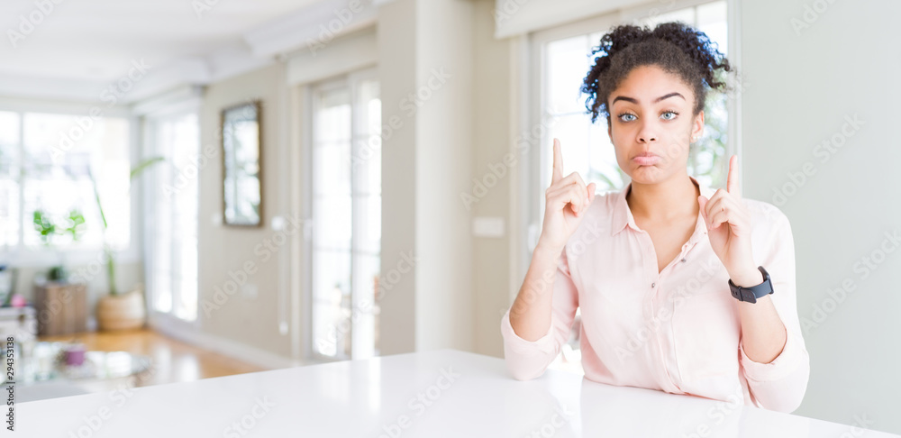 Wide angle of beautiful african american woman with afro hair Pointing up looking sad and upset, indicating direction with fingers, unhappy and depressed. Wide angle of beautiful african american woman with afro hair Pointing up looking sad and upset, indicating direction with fingers, unhappy and depressed.