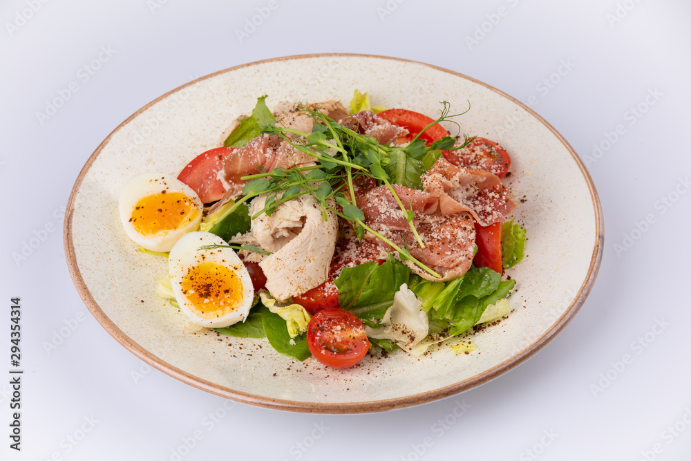a bowl of fresh lettuce salad with tomatoes eggs prosciutto over white.
